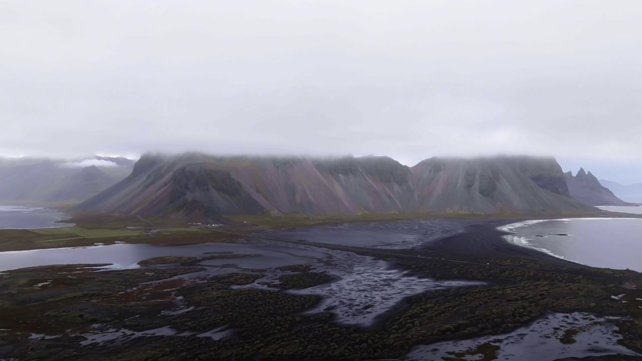 Luftfoto bakover foran den tåkete Vestrahorn-toppen, i Stokksnes, Island