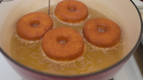 Four-donuts-deep-fry-in-yellow-oil,-Slow-Motion-Closeup-from-Above