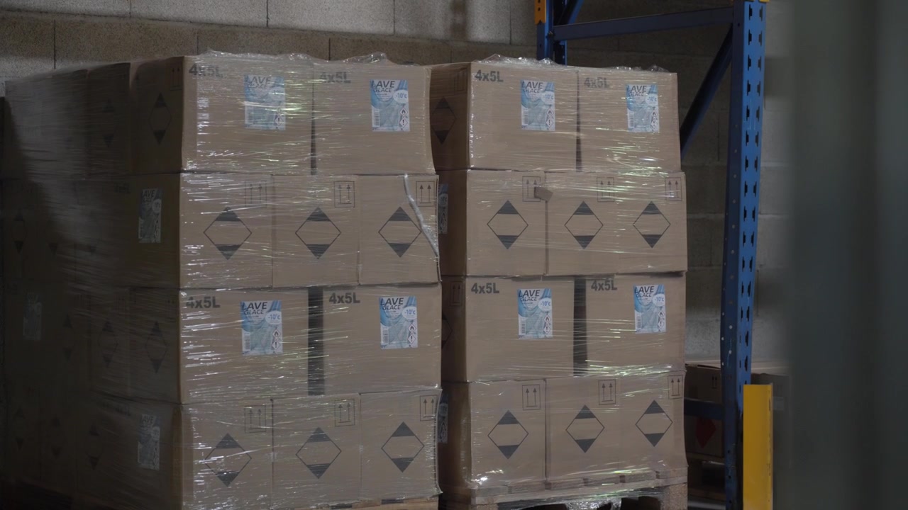 Stacked coolant product boxes wrapped on pallets inside factory warehouse, reveal past pole