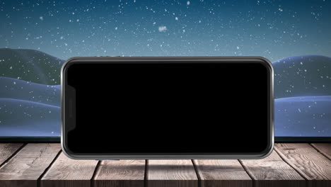 Animation-Eines-Leeren-Smartphone-Bildschirms-Mit-Winterlandschaft-Und-Schnee,-Der-Auf-Eine-Holzoberfläche-Fällt