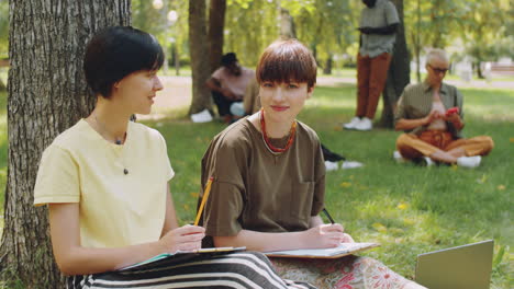 portrait of two positive college girls studying outdoors in park