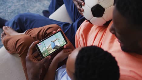 composite of father and son at home watching athletics discus event on smartphone