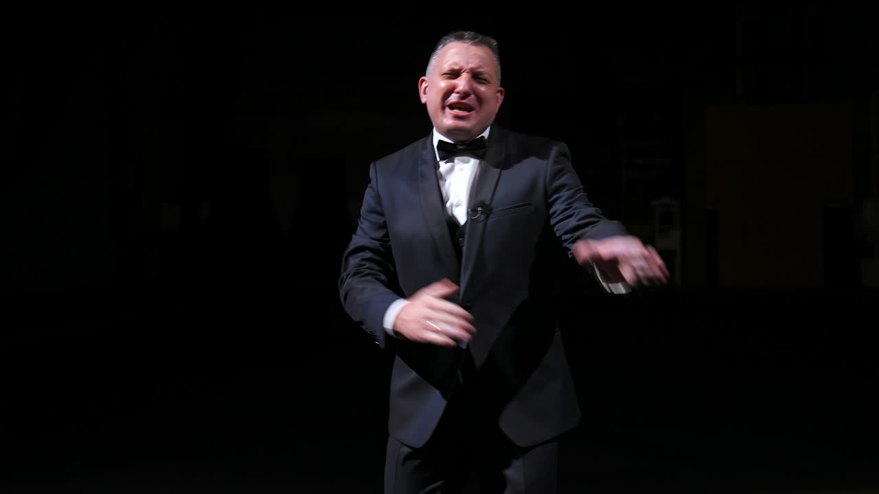 Man is speaking in the light of the floodlights standing on stage to the camera. Actor, artist on performance. Activ gestures with hands.