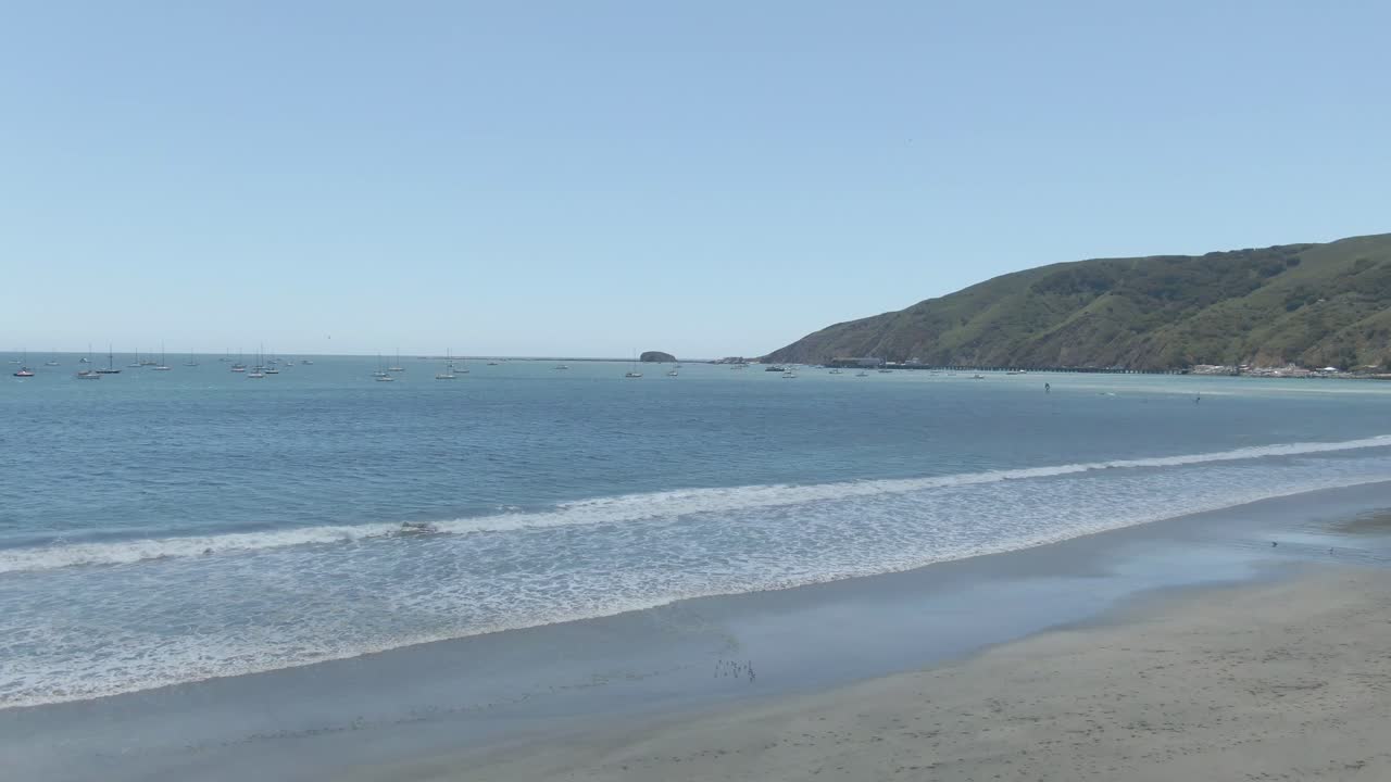 A smooth, sweeping aerial pan across the rugged coastline of Avila Beach, California. This high-resolution 4K clip showcases the vast Pacific horizon, gentle ocean swells, and the scenic transition