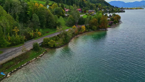 Dolly-Aéreo-A-Lo-Largo-De-La-Costa-Del-Lago-Con-Exuberantes-Y-Vibrantes-Laderas-Verdes-De-Hierba-Y-árboles,-Casas-Con-Vistas-Al-Agua