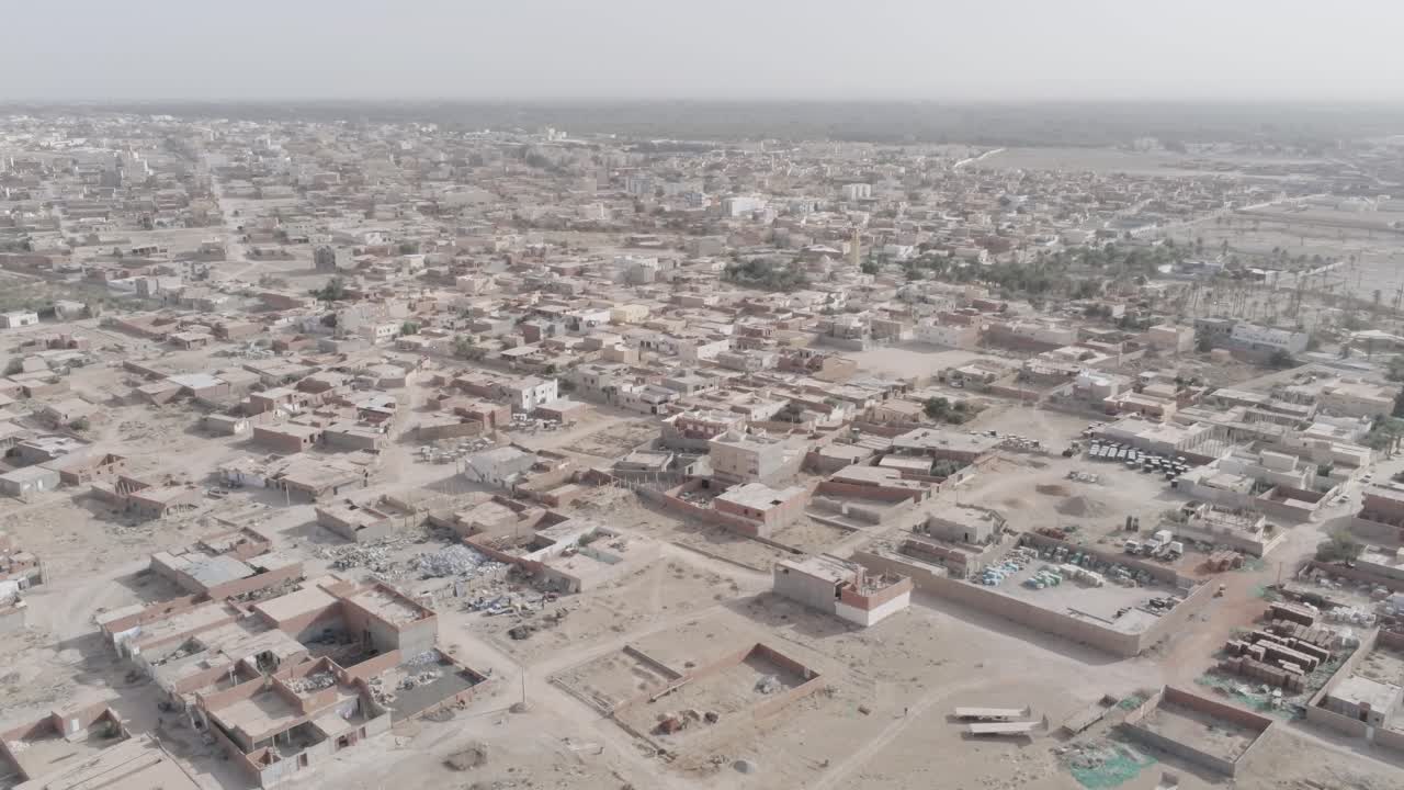 Drönarfilm som fångar en tunisisk stad i en halvtorr ökenregion, visar bostadsområden och spridd grönska.