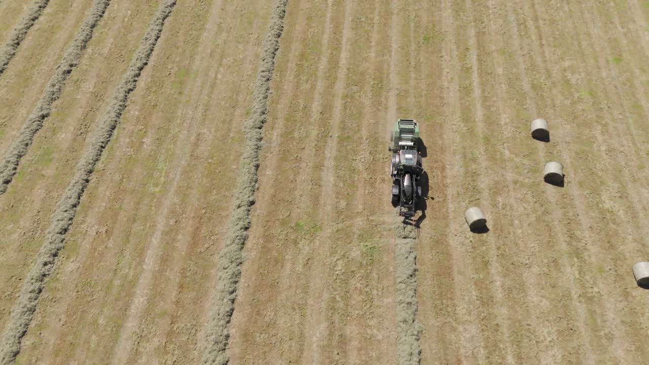 굴곡 된 언덕 으로 둘러싸인 큰 농장 에서 신선 한 잔디 를 정식 으로 수확 하고 어 놓기 위해 준비 하는 트랙터 의 공중 추적 모습