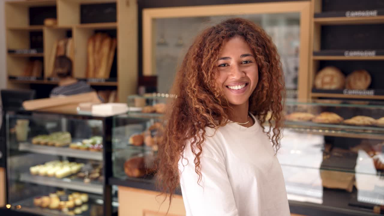 Giovane donna amichevole con i capelli ricci che sorride in una panetteria.