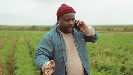 african american farmer standing with shovel on field and talking on phone