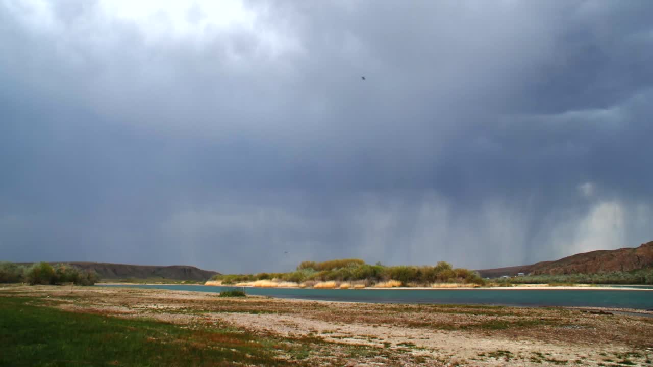 Captivating time-lapse: Summer rainstorm over the fast-flowing river with majestic mountains, creating a dusty and arid atmosphere. Moody sky, rain clouds.