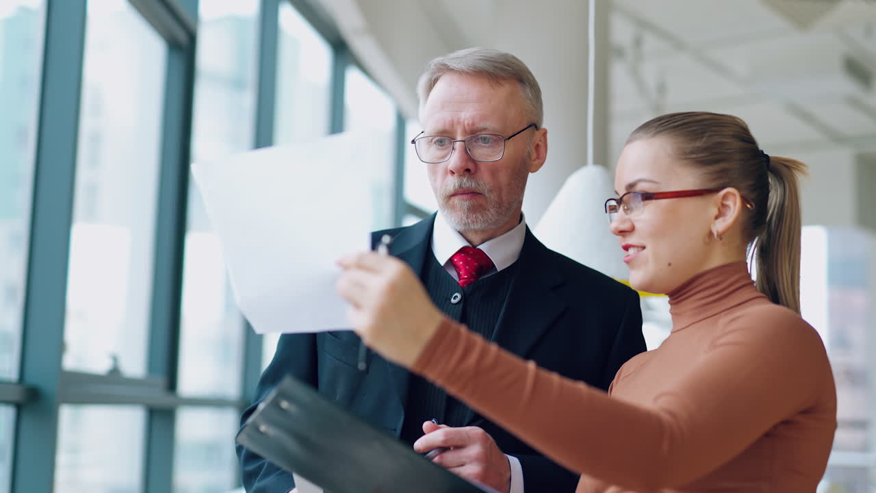 Smart secretary talks to her boss. Mature businessman in costume listening to the young woman showing documents in the office.