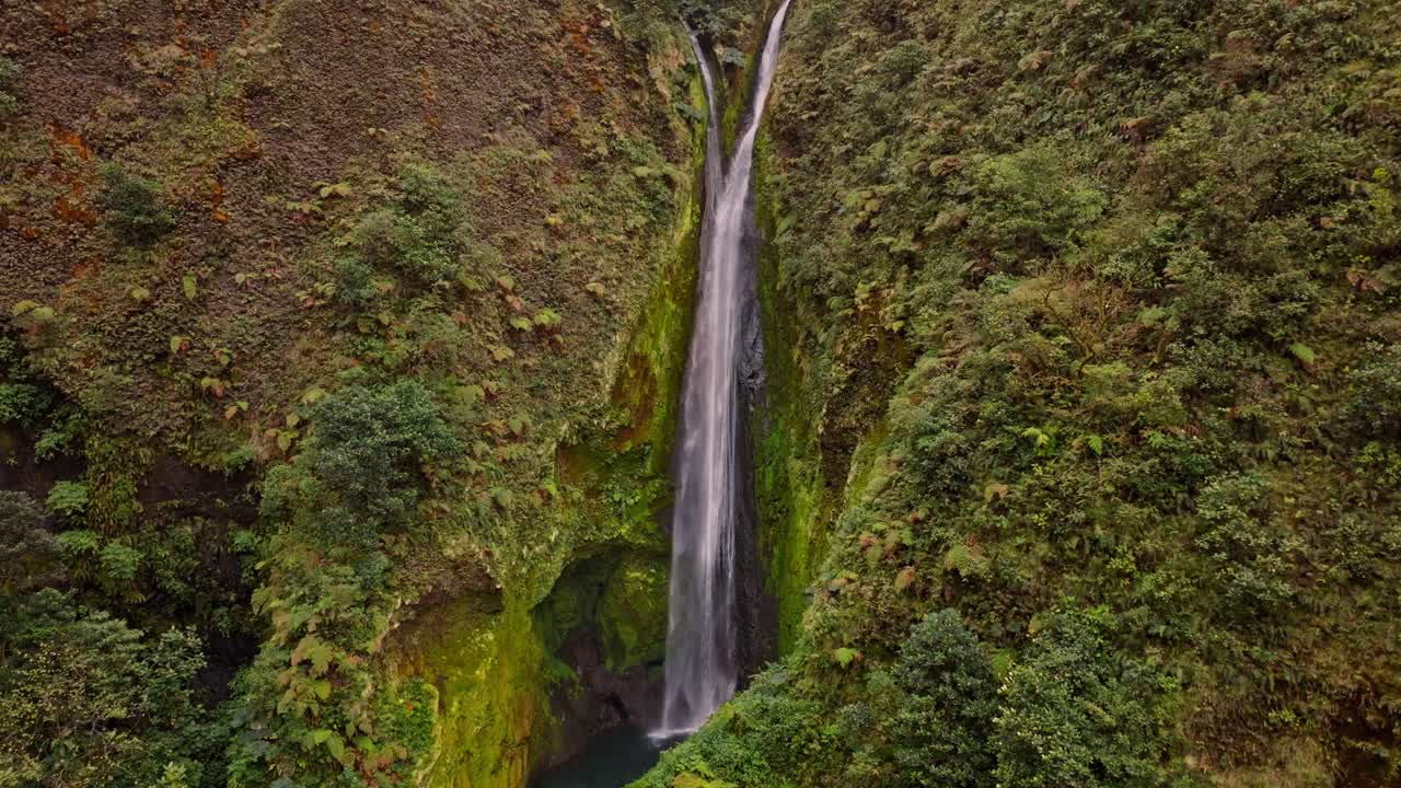 An breathtaking aerial view reveals the unique and beautiful Vuelta al Cañon waterfall, cascading majestically into a vibrant, untouched green canyon