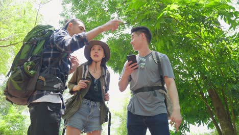 group of asian backpacker people have fun travel in forest together. attractive man and woman friend walking and looking at map on mobile phone to find direction during holiday vacation trip on summer