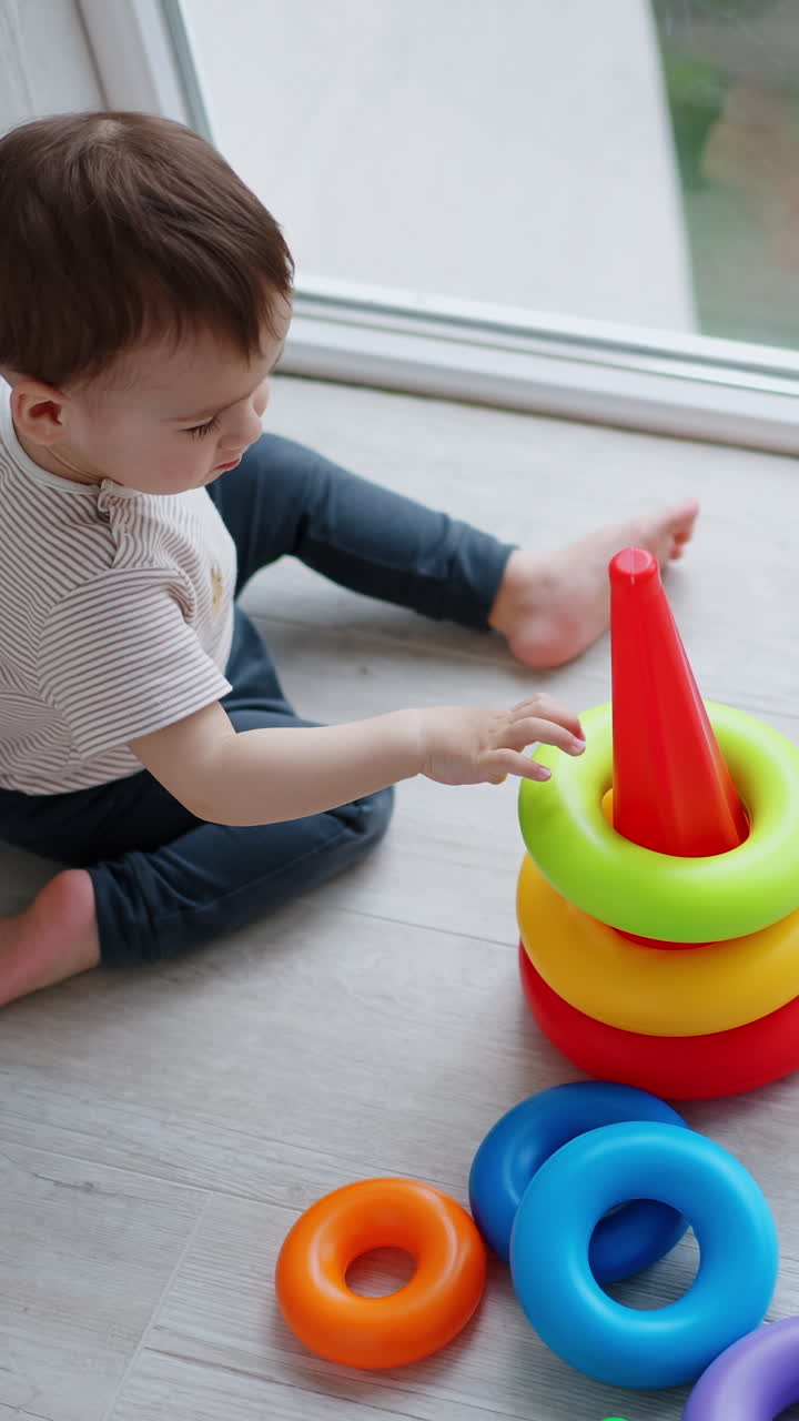 Lovely Caucasian child puts colorful rings on the base. Baby boy playing with toy pyramid. Top view. Vertical video
