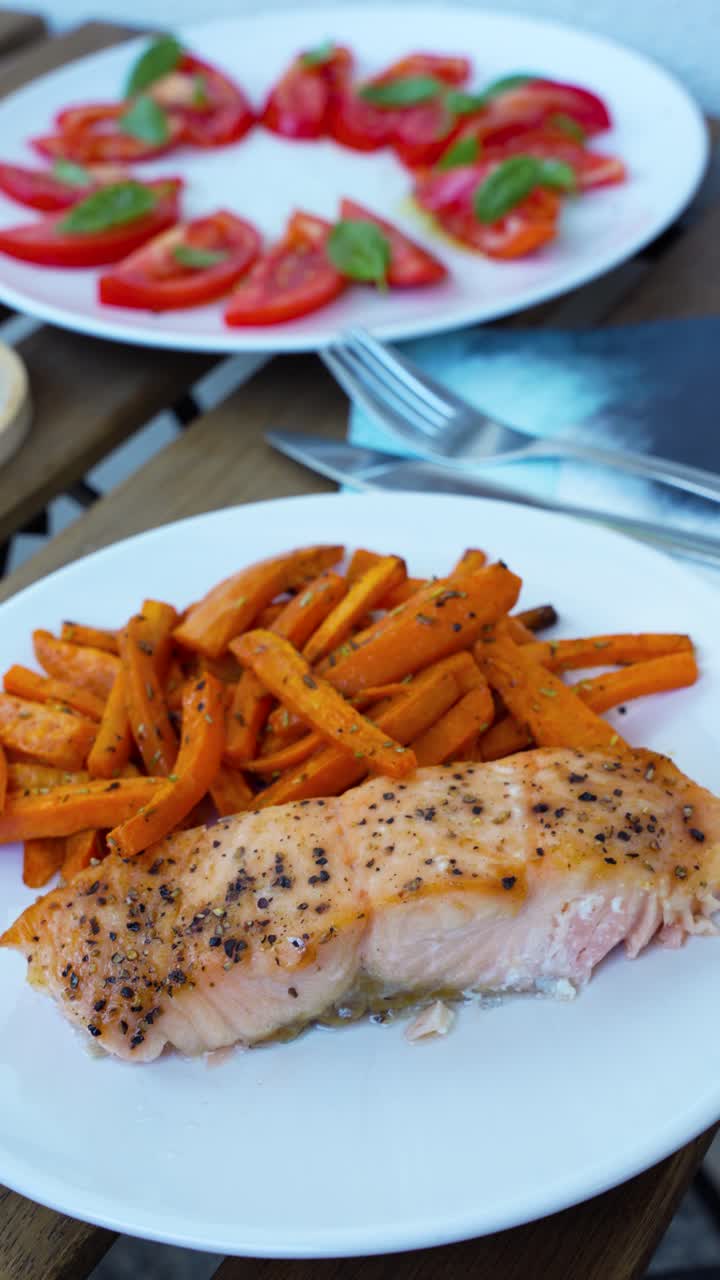 Tasty meal of salmon with sweet potato fries, tomato salad, and wine. Vertical