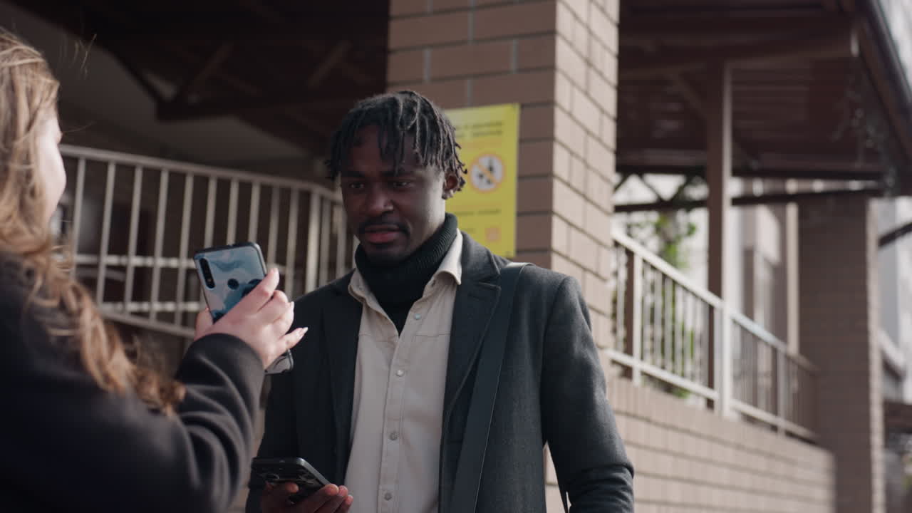 En kollega skynder sig mod indgangen, vinden løfter håret, mens et tjek af telefonen bekræfter et møde, hvilket får vedkommende til hurtigt at bevæge sig ned ad trappen. En urban baggrund viser murstensvægge, en skyggefuld gang og en mild følelse af travlhed.