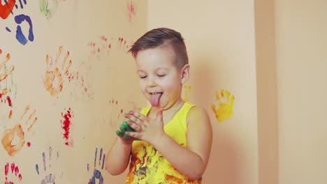 Niño-Pequeño-Con-Camisa-Amarilla-Sin-Mangas-Mostrando-La-Lengua.-Sus-Manos-Están-Sucias-De-Colores.-él-Está-Viviendo-Sus-Huellas-En-La-Pared