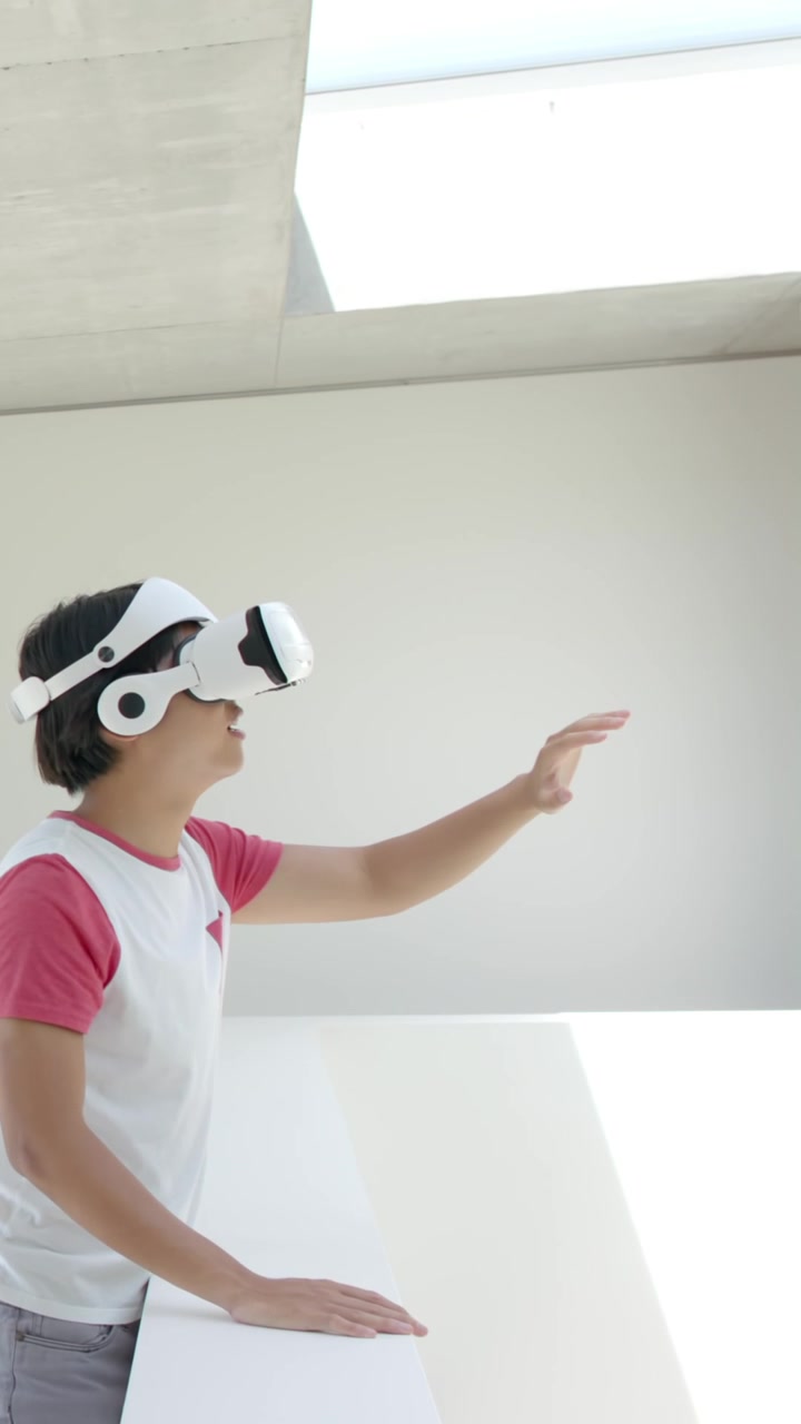 Video verticale: Uomo asiatico con visore VR che si protende verso il tavolo dopo un segnale VR vicino al lucernario, con spazio per il testo.