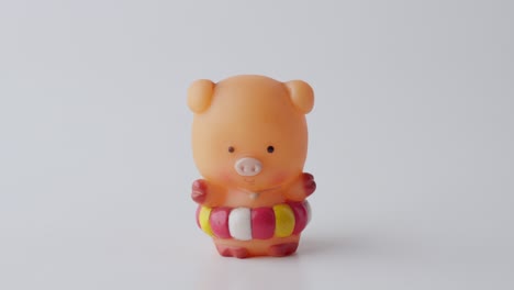 Hand-Holding-Placing-Small-Plastic-Rubber-Piggy-Toy-Figure-On-White-Surface,-Close-Up