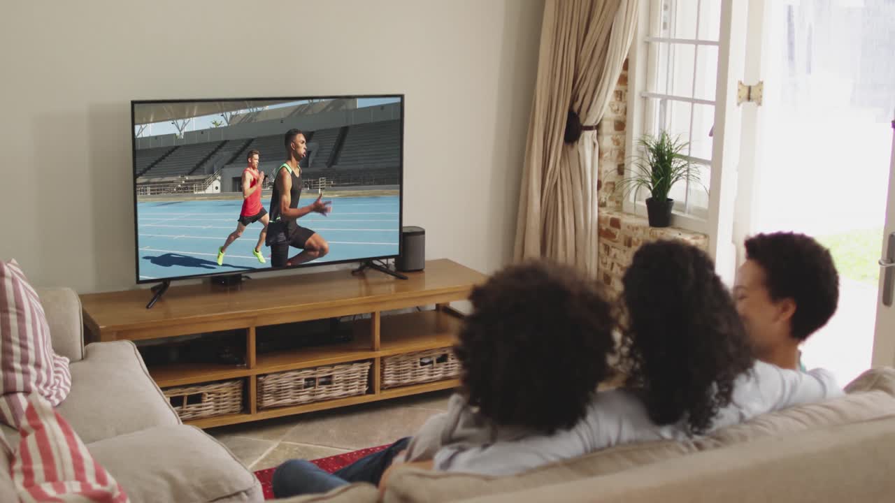 Composizione di famiglia felice seduta insieme a casa che guarda un evento di atletica leggera di corsa in TV.