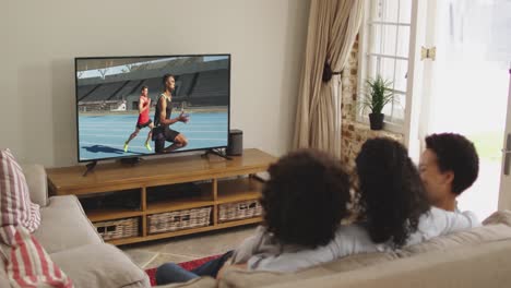 composite of happy family sitting at home together watching running athletics event on tv