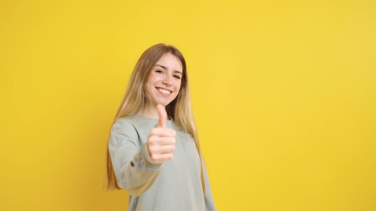 Young woman showing thumbs up on yellow background