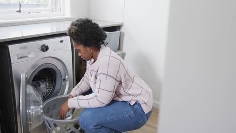 african american woman putting clothes into washing machine, doing laundry at home, slow motion