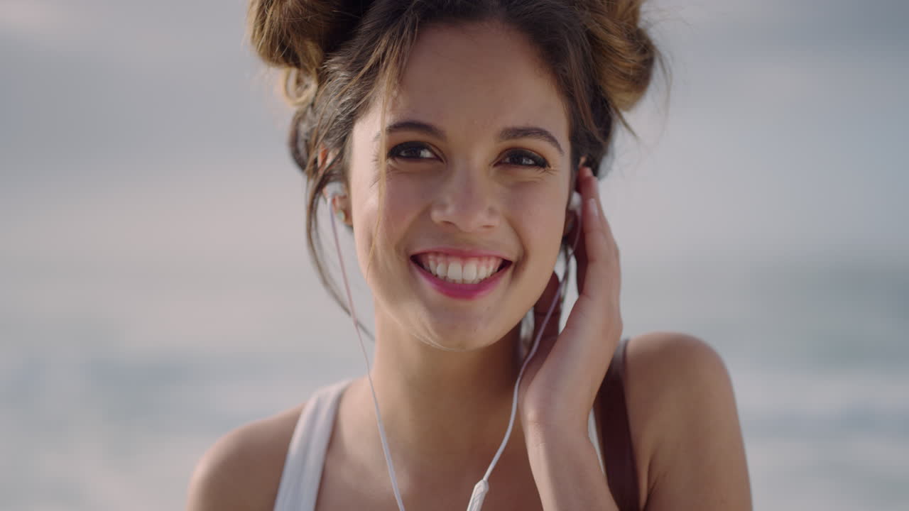 retrato en primer plano de una joven feliz con auriculares sonriendo disfrutando escuchando música en la playa hermosa chica hispana en cámara lenta