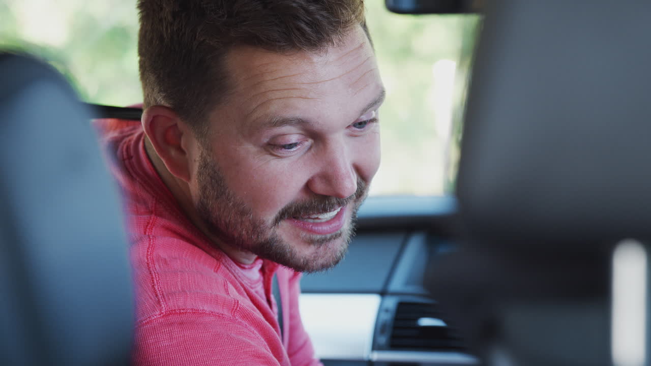 Father Turning Round To Talk To Children In Back Seat On Car Journey