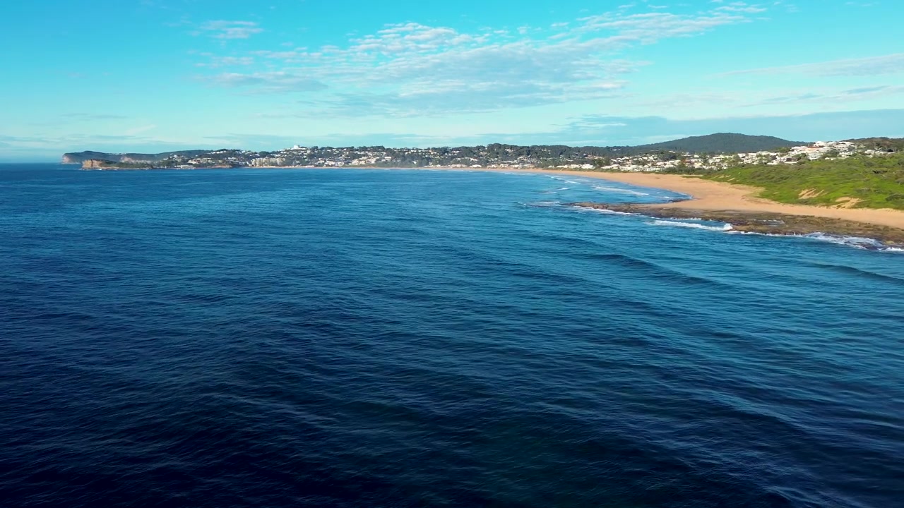 Paesaggio aereo ripreso da drone della superficie dell'acqua dell'oceano lungo una costa sabbiosa con un promontorio di una città rurale e nuvole soffici nel cielo a Spoon Bay Wamberal Central Coast NSW Australia turismo naturalistico