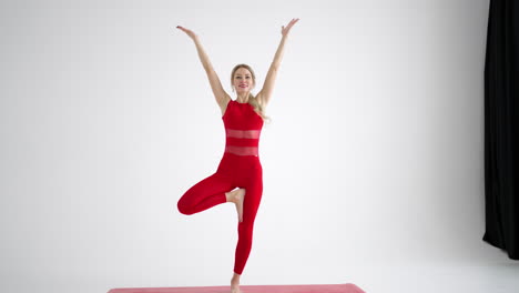 a woman in a red tracksuit looking into the camera conducts training and tells and shows exercises from yoga or pilates on a white background. yoga instructor shows exercises for home classes