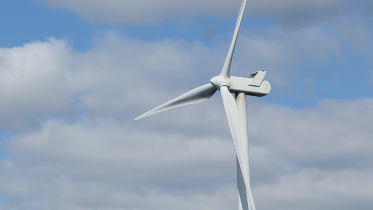 Large wind turbine slowly spinning outdoors, daylight, static camera, blue sky with scattered clouds