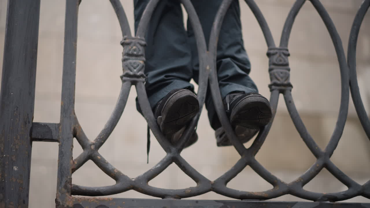 Relaxed girl on city bridge. Playful woman balancing on concrete ledge. Casual young woman hanging feet over bridge railing. An easygoing woman swings her legs above rainy city pavement