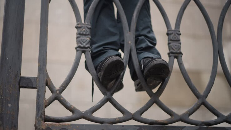 Relaxed girl on city bridge. Playful woman balancing on concrete ledge. Casual young woman hanging feet over bridge railing. An easygoing woman swings her legs above rainy city pavement