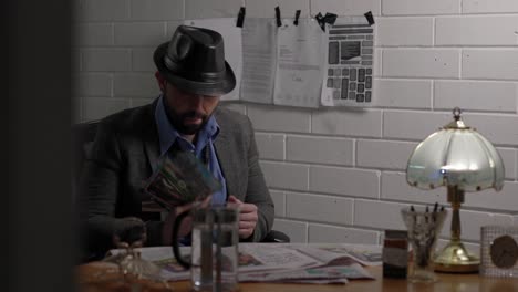 man police detective in jacket and hat sitting at station desk looking at papers documents