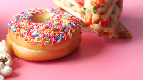 colorful sprinkled donut, pizza slice, and popcorn on pink background