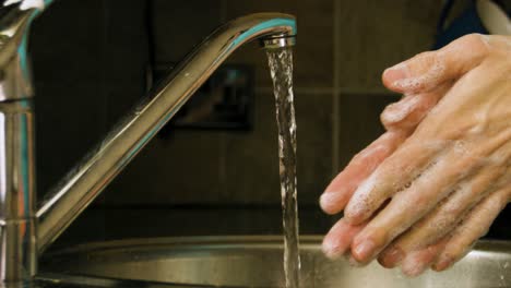 lavarse las manos jabonosas y enjuagarse con agua en un fregadero de cocina casero a cámara lenta