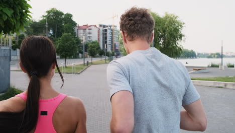 back view of a young couple running together in an urban park in the city near a river