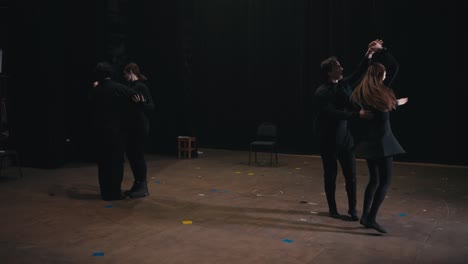 two pairs of confident actors in black suits dance on stage during their rehearsal for a play in the theater. careful preparation of actors in black suits before performing and dancing in the theater