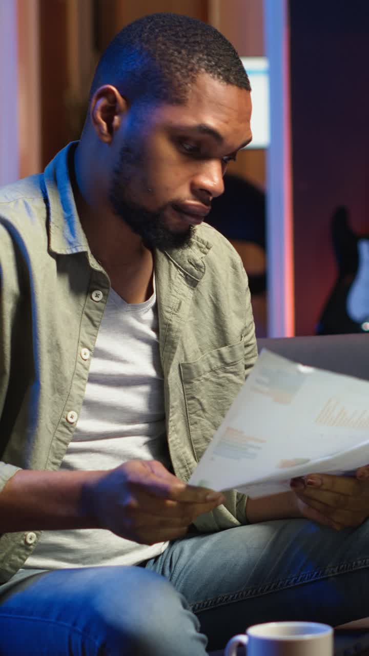 Vertical Video Young adult sitting on couch and reading research papers with analytics