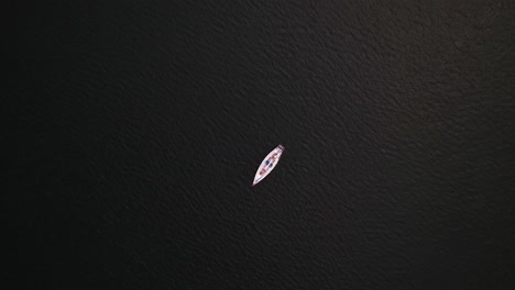 drone descending to a single white sailboat in the middle of the open ocean