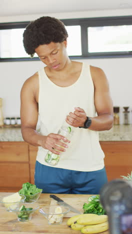 video vertical de un hombre afroamericano sonriente preparando una bebida para la salud en la cocina