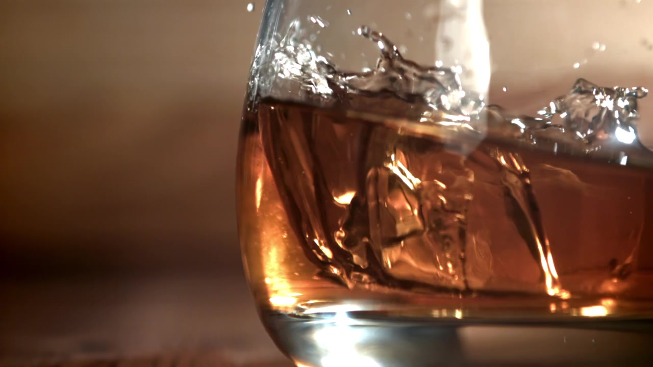 Cubetto di ghiaccio che cade in un bicchiere di whisky al rallentatore