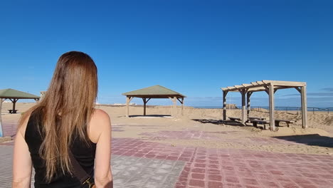 girl with long hair walks towards the beach in casa del mar, tarfaya,, marroco. elegant beautiful girl overlooking the bay. beautiful girl walks with her back to the camera