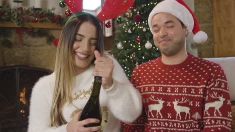 Junges-Paar-öffnet-Eine-Flasche-Champagner-Während-Des-Weihnachtsvideoanrufs