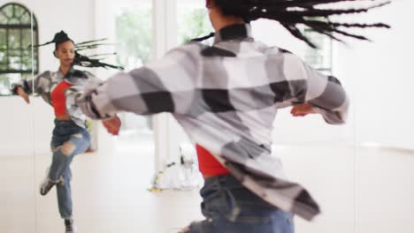 biracial female dancer dancing alone in front of mirror in dance studio, slow motion