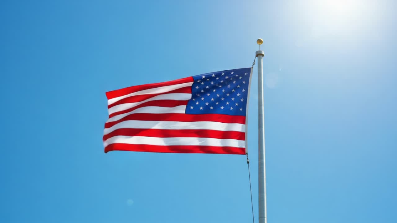 The American Flag Waving Gracefully Against a Clear Blue Sky, Symbolizing Freedom and Patriotism in a Bright Sunlit Atmosphere