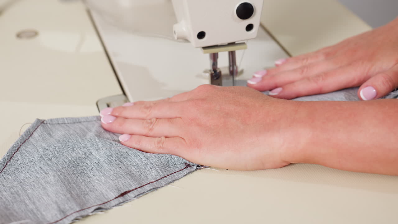 Hand view of stylist carefully sewing apparel through needle, adjusting fabric with precise handling, focusing on stitching accuracy, ensuring garment alignment, showing professional skill
