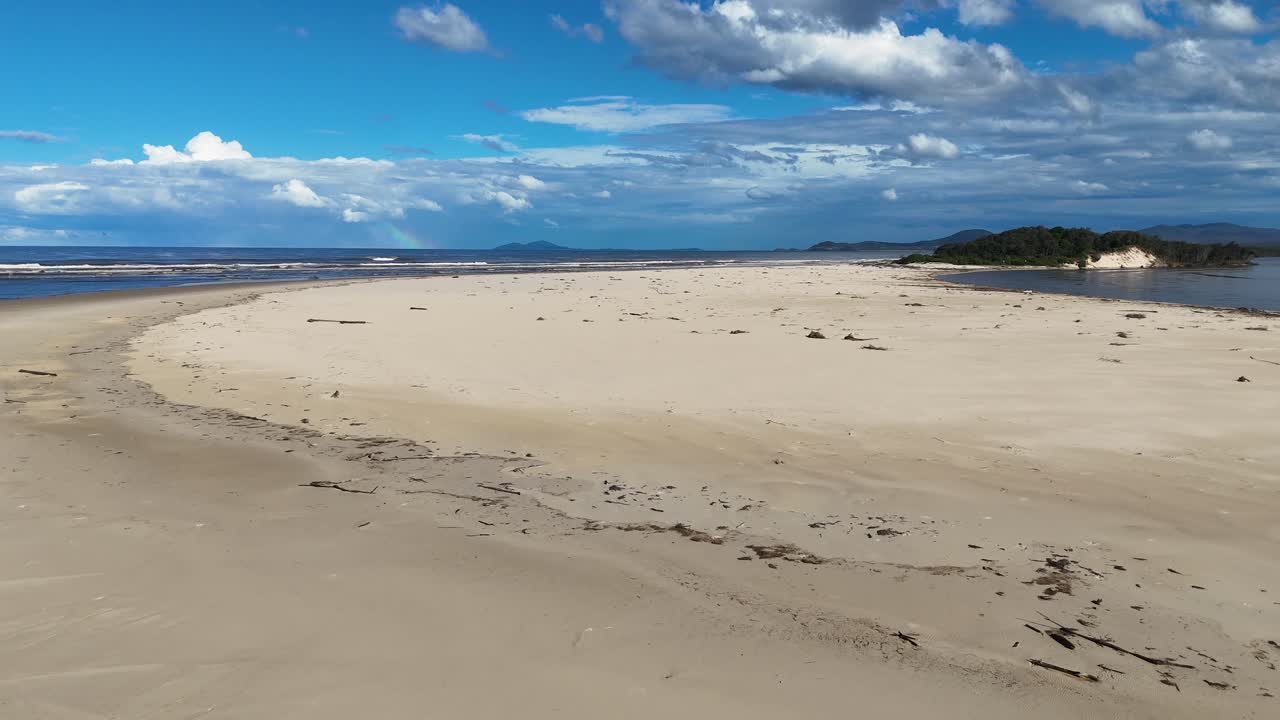 Wide-angle daytime pan of tranquil, empty sandy beach with dunes and blue sky in sunlight