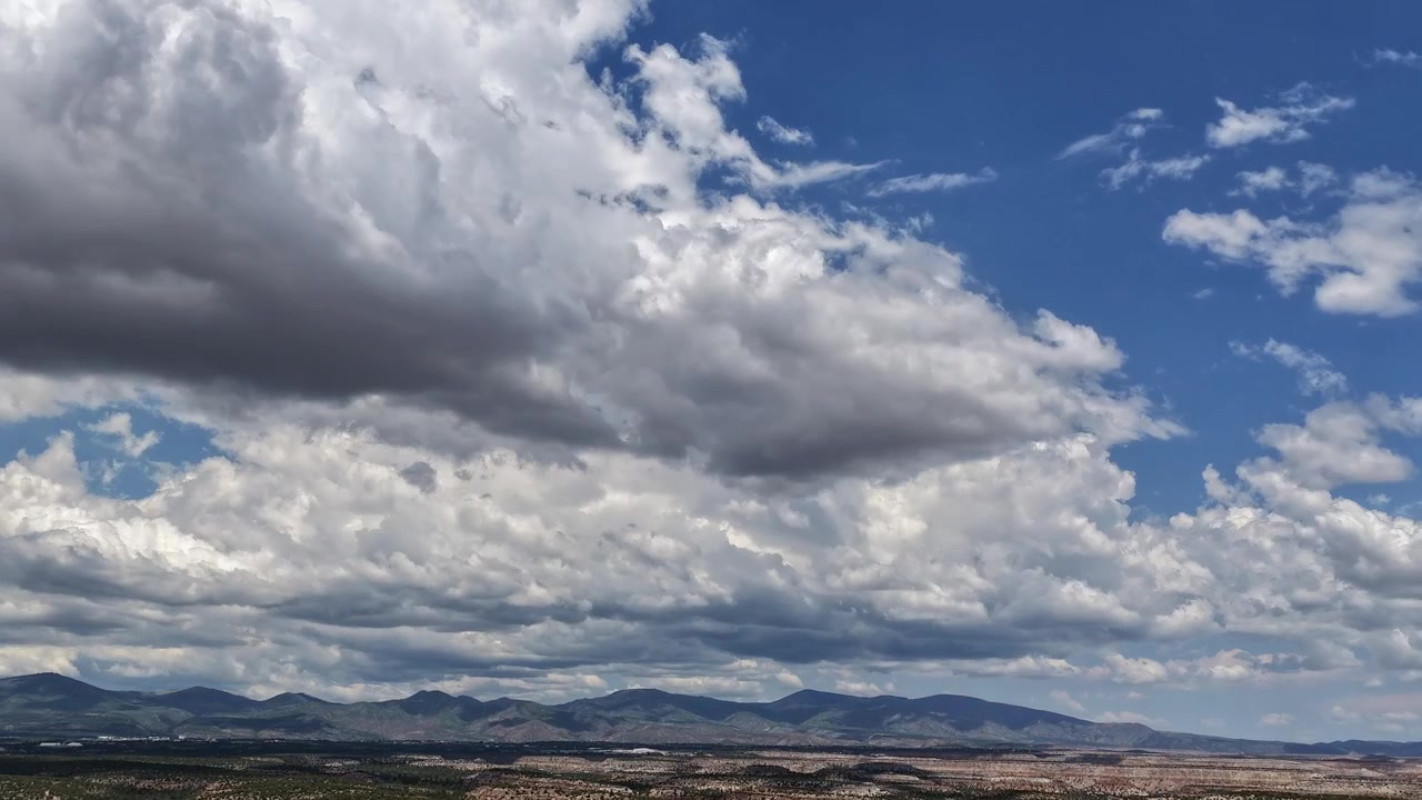 Timelapse 4K con drone di nuvole temporalesche in rapido movimento che spazzano un vasto paesaggio desertico d'alta quota. Ombre scure e profonde contrastano con cumuli bianchi e luminosi sull'orizzonte montuoso